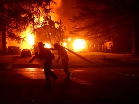 Los Angeles County firefighters pull a hose in front of a burning home as the Eaton Fire moved through the area in Altadena, Calif., on Jan. 8.
