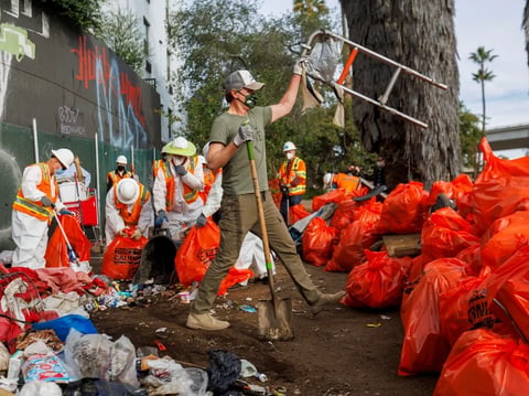 Gov. Gavin Newsom helps cleanup a homeless encampment along a freeway in San Diego, on Jan. 12, 2022.