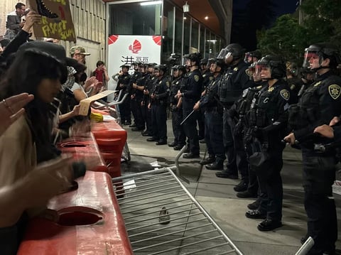 Students chant and bang on the barricades outside UC Berkeley's Zellerbach Hall as campus police officers stand with batons raised outside the Turning Point USA "American Comeback Tour" event on Nov. 10, 2025.