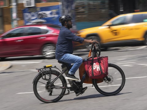 A delivery worker rides a motorized bicycle in New York, Tuesday, July 25, 2023.