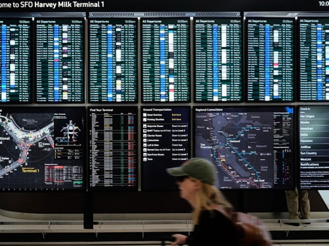 A traveler walks past screens showing outgoing and incoming flights at San Francisco International Airport ahead of the Memorial Day holiday weekend in San Francisco, Thursday, May 22, 2025.