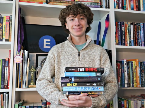 Ethan Minton stands with a stack of his favorite books he's collected over the years. He's the host of the podcast E Train Talks where he interview's authors and reviews books.