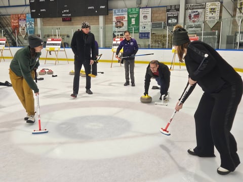 Ben Skyrme (center) gets ready to throw his stone as Isabelle Romero (left) and Lynne Skyrme (right) prepare to sweep during a Wine Country Curling Club class at Skatetown Ice in Roseville Feb. 15, 2026. (Sarit Laschinsky/CapRadio)