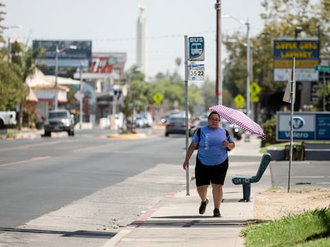 A Fresno resident uses an umbrella to shield herself from the sun on Aug. 30, 2022, as a heat wave descended over California.