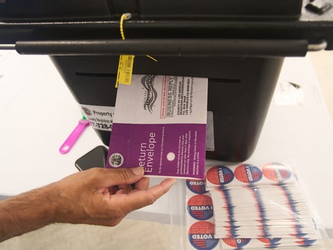 Los Angeles County election worker Richard Arias, deposits a ballot envelope after checking for written name and signature, as people vote in person on California's Prop 50 election at the Los Angeles County Registrar-Recorder's office Oct. 29, 2025.