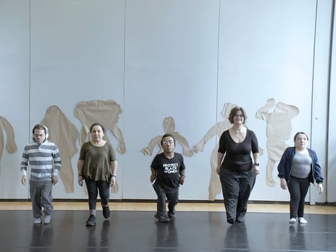 Participants in the "How We Look" creative workshop series walk away from their body tracings on the wall.