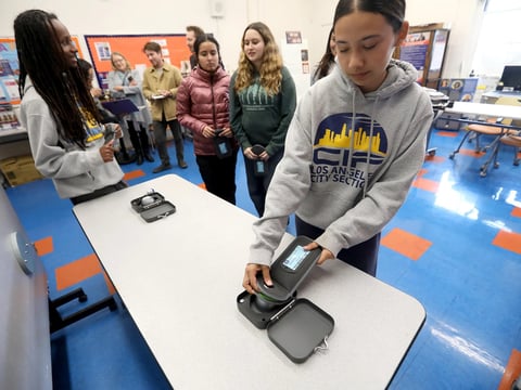Senior Angie Mendoza demonstrates how to demagnetize the Yondr pouch to unlock her smartphone at University High School Charter in Los Angeles on March 6, 2025.