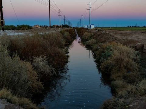 An irrigation ditch runs between farm land, on the right, and a proposed 950,000-square-foot data center, on the left, in Imperial County on March 11, 2026.