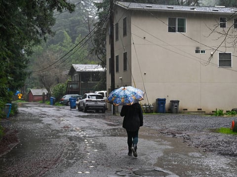 A woman with an umbrella walks on a road during heavy rain in Guerneville, California, on Feb. 6, 2025, as an atmospheric river hits Northern California.
