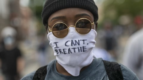 Protests over police treatment of black people have sparked concerns about the spread of COVID-19. Here, a protester marches Monday in Philadelphia with a cloth mask saying, "I can't breathe."