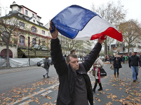A man displays the French flag in front of the Bataclan concert hall, which was a site of last Friday's attacks, in Paris, Tuesday, Nov. 17, 2015. France is demanding security aid and assistance from the European Union.