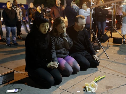 A group prays near the site of a warehouse fire Sunday, Dec. 4, 2016, in Oakland, Calif. 