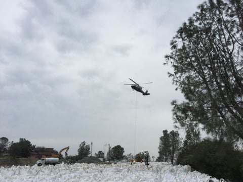 A helicopter prepares to lift a large bag of rocks to be used at the base of the Oroville Dam emergency spillway.