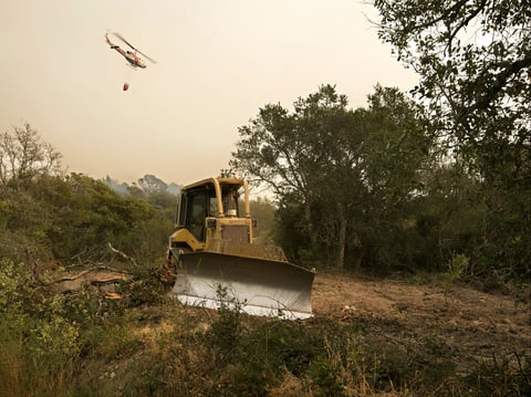 A bulldozer is used to cut a fire break as a helicopter flies over with a bucket of water to fight the flames of a massive wildfire Thursday, Oct. 12, 2017, in Sonoma, Calif.