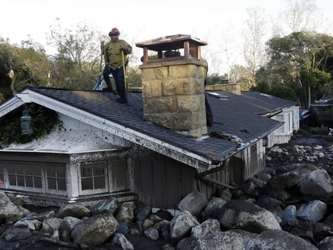 A firefighter stands on the roof of a house submerged in mud and rocks Wednesday, Jan. 10, 2018, in Montecito, Calif.