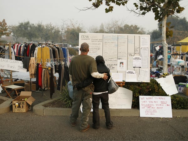 Tera Hickerson, right, and Columbus Holt embrace as they look at a board with information for services at a makeshift encampment outside a Walmart store for people displaced by the Camp Fire, Friday, Nov. 16, 2018, in Chico, Calif.