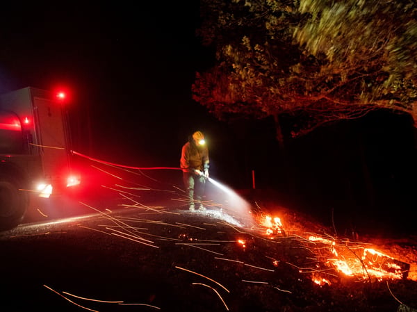 A firefighter battling the Kincade fire extinguishes a hot spot as strong winds send embers flying in Calistoga, Calif., on Tuesday, Oct. 29, 2019.