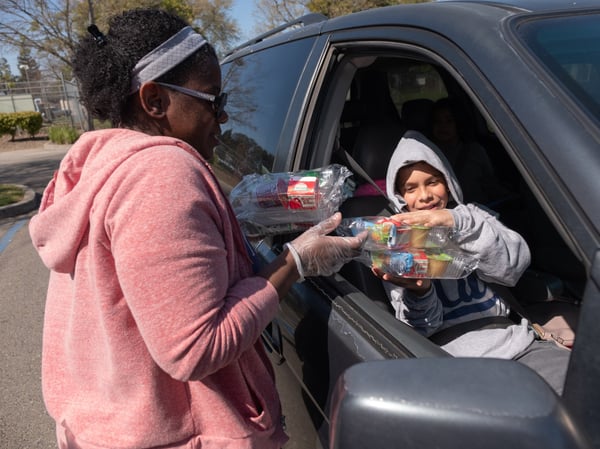 Food and Nutrition Lead Stacey McDuffie hands a prepackaged lunch and tomorrow's breakfast to Hector Corrasco, 12, and his siblings in the car as part of the "drive-through" meal distribution at Florin Elementary School.