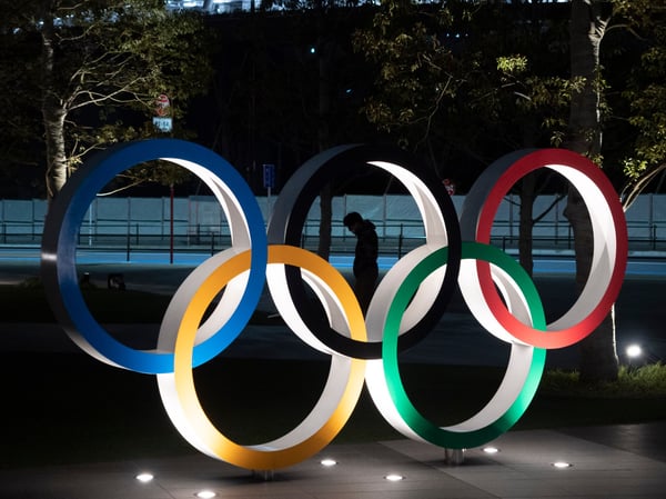 A man is seen through the Olympic rings in front of the New National Stadium in Tokyo, Tuesday, March 24, 2020.