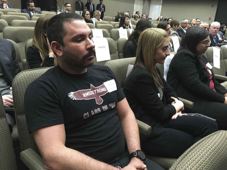 Shane Fedderman, left, a 1998 graduate of Marjory Stoneman Douglas High School in Parkland, Fla., watches as families of mass shooting victims urge California's public pension funds to stop investing in retailers of assault weapons in Sacramento.