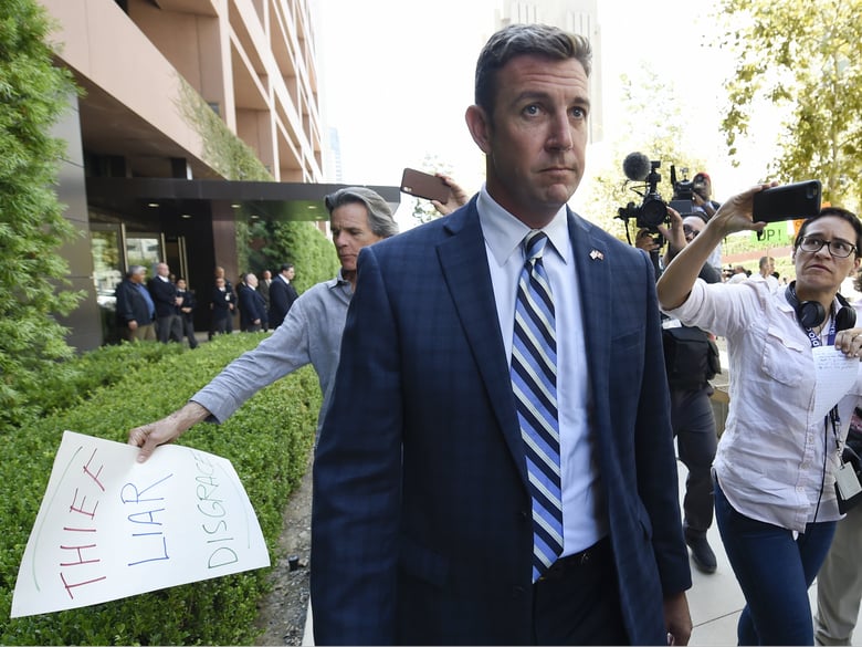 U.S. Rep. Duncan Hunter, center, leaves an arraignment hearing as a protester carries a sign, left, Thursday, Aug. 23, 2018, in San Diego. 