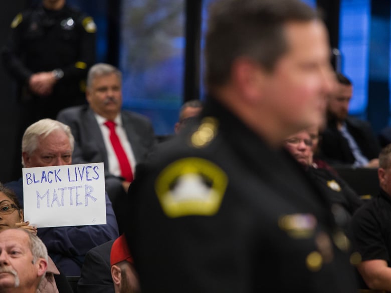 A protester holds a sign while Sacramento Sheriff Scott Jones speaks at the county Board of Supervisors meeting Dec. 4, 2018.