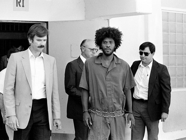 In this July 31, 1983, file photo, Kevin Cooper, center, a suspect in connection with the slashing death of four people in Chino, is escorted to a car for transport to San Bernadino from Santa Barbara, Calif.