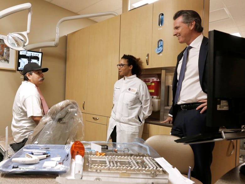 Gov. Gavin Newsom, right, talks with dental patient Arthur Hernandez, left, as he tours the Sacramento Native American Health Center with Dental Director Vanessa Franks, center, in Sacramento, Calif., Tuesday, July 9, 2019.