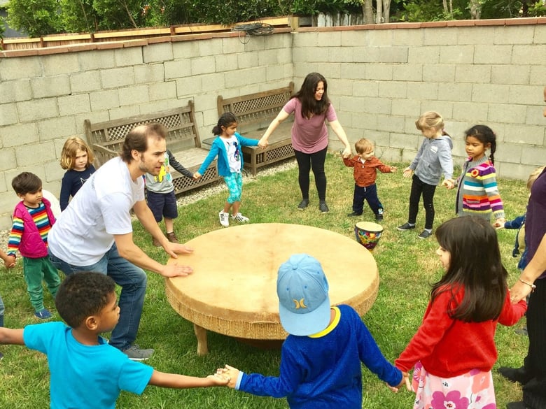 Children at Little Stars Preschool and Family Childcare in Los Angeles dance at a drum circle with the school’s owner/director Darlene Morales, at top in the pink t-shirt.