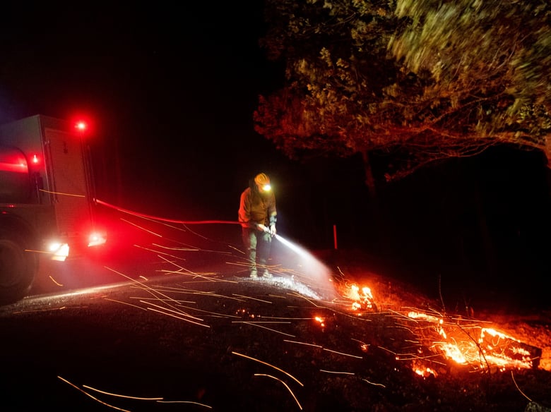 A firefighter battling the Kincade fire extinguishes a hot spot as strong winds send embers flying in Calistoga, Calif., on Tuesday, Oct. 29, 2019.