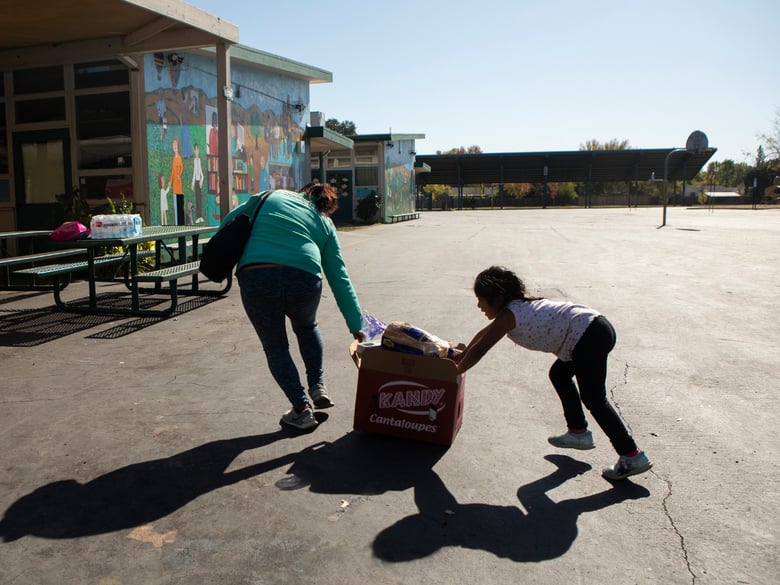 A mother and daughter push a crate of food across the El Verano Elementary School yard during a food distribution for families affected by October's planned power outages.