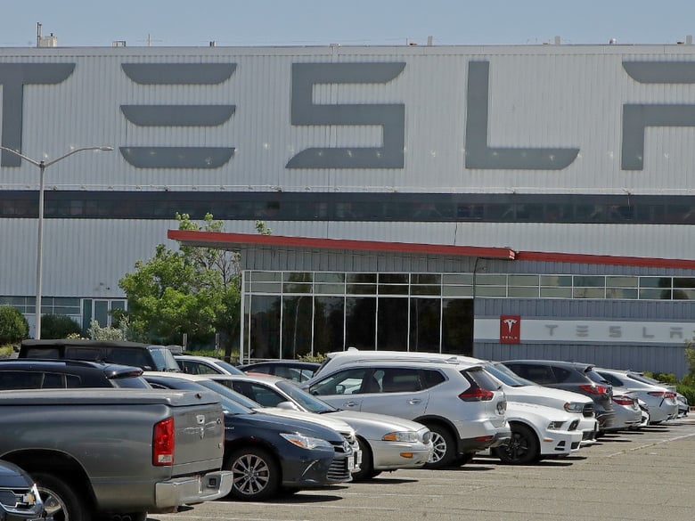 A masked man walks in the Tesla plant parking lot Monday, May 11, 2020, in Fremont, Calif. The parking lot was nearly full at Tesla's California electric car factory Monday, an indication that the company could be resuming production.