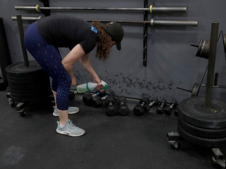 Alexis Garrod, CrossFit Potrero Hill partner and head coach, cleans off weight training equipment after instructing a class over Zoom in an empty gym, which closed for shelter in place orders over COVID-19 concerns, in San Francisco, Friday, April 24