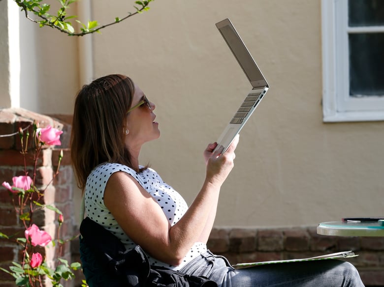 Kelly Dighero, a 3rd grade teacher at Phoebe Hearst Elementary School, holds up her laptop to block the sun during her first online meeting with students and parents on the front lawn of her home in Sacramento. April 13, 2020