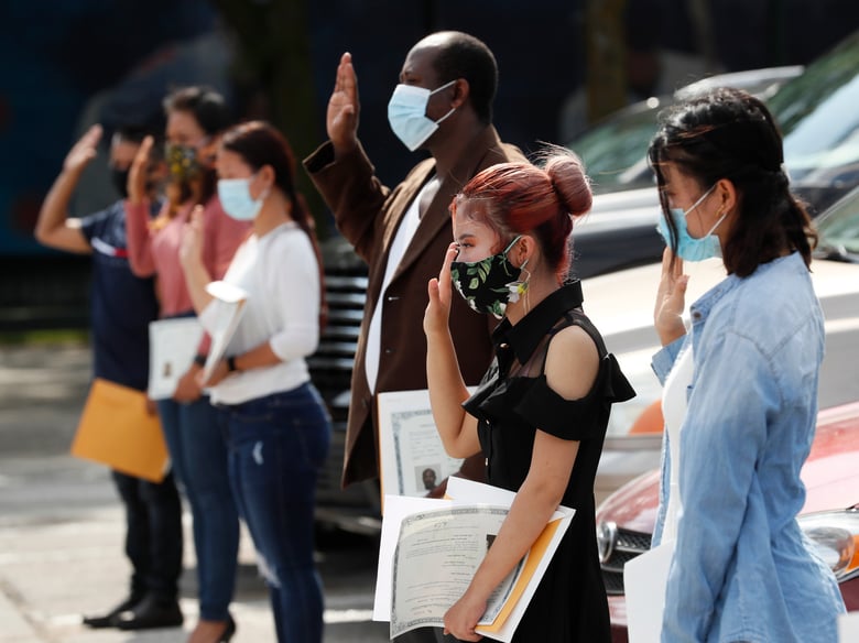 People raise their hands while taking the Oath of Allegiance during a drive-thru naturalization ceremony at Principal Park, Friday, June 26, 2020, in Des Moines, Iowa.