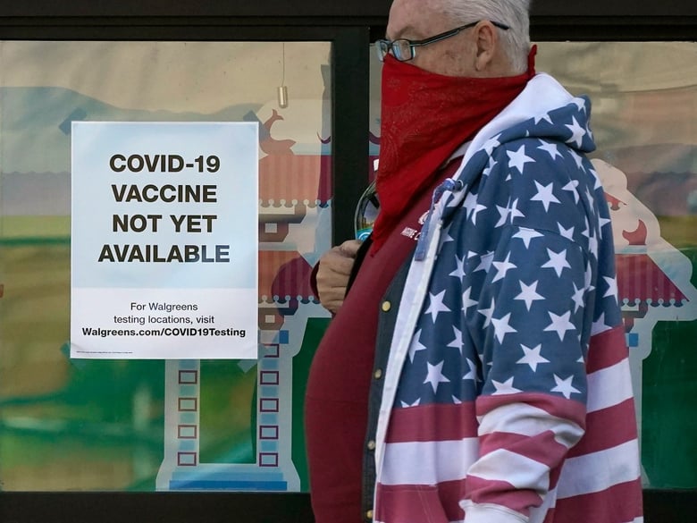 A pedestrian wearing a mask walks past a sign advising that COVID-19 vaccines are not available yet at a Walgreen's pharmacy store during the coronavirus outbreak in San Francisco, Wednesday, Dec. 2, 2020.