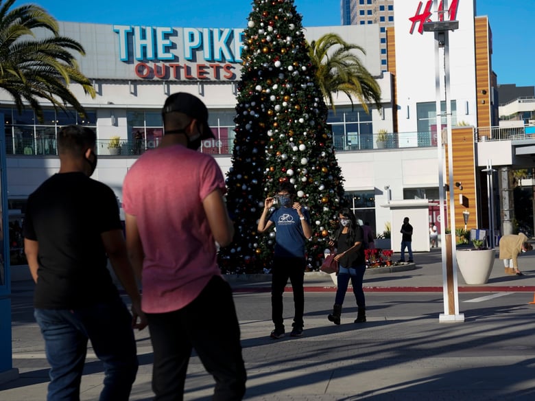 Shoppers wearing face masks walk past a Christmas tree at The Pike Outlets Saturday, Dec 26, 2020, in Long Beach, Calif.