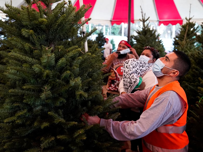 Robert Navarro, right, helps customers choose a Christmas tree while wearing a mask on Tuesday, Dec. 1, 2020, in Long Beach, Calif