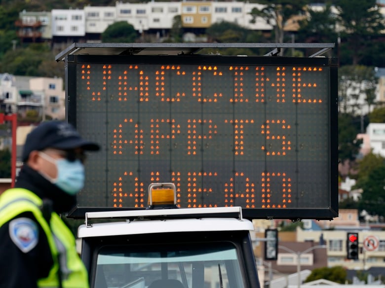 An officer stands in front of a sign advising of vaccine appointments at a drive-up vaccination center at City College of San Francisco during the coronavirus pandemic in San Francisco, Monday, Feb. 1, 2021.