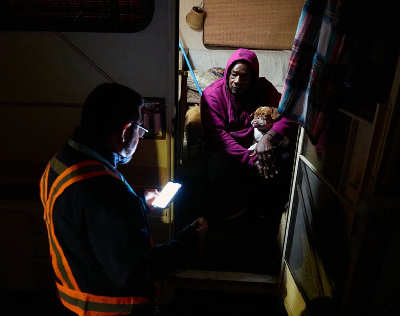 Eric Guerra, a member of the Sacramento city council (l) talks with Charlie Sims and his dog Devo in the doorway of the motorhome they live in during the Point-in-Time (PIT) count of people experiencing homelessness Jan. 24, 2024.