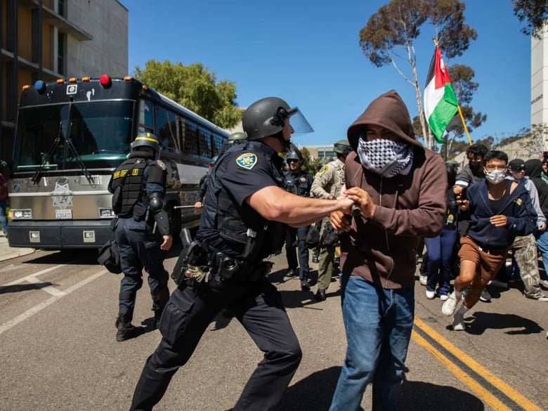 A University of California campus police officer pushes a pro-Palestinian protester away from a moving San Diego Sheriff's bus with arrested protesters onboard at UC San Diego in San Diego on May 6, 2024. Photo by Adriana Heldiz, CalMatters