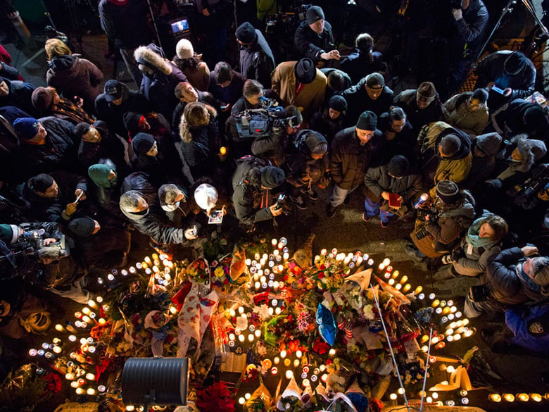 Mourners, members of the media and other gather at a memorial Sunday, Dec. 21, 2014, near the spot where two New York Police Department officers, sitting inside a patrol car the previous day, were shot by an armed man, killing them both.