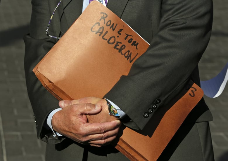 FILE - In this Feb. 24, 2014 file photo, Department of Justice Public Affairs Officer Thom Mrozek holds a folder tagged with the names of California State Sen. Ron Calderon and his brother Tom Calderon during a news conference in Los Angeles.