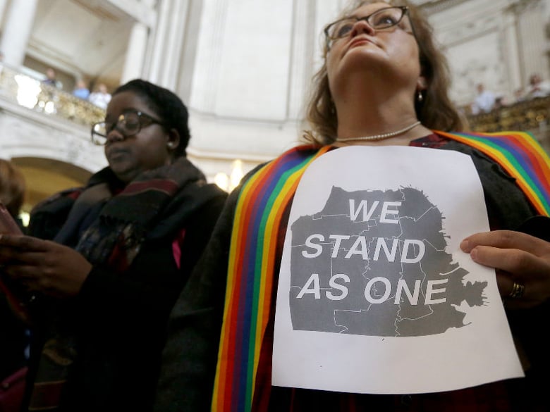 The Rev. Annie Steinberg-Behrman, right, provisional pastor with Metropolitan Community Church, holds a sign while listening to speakers at a meeting at City Hall in San Francisco reaffirming the city's Sanctuary status. Nov. 14, 2016. 