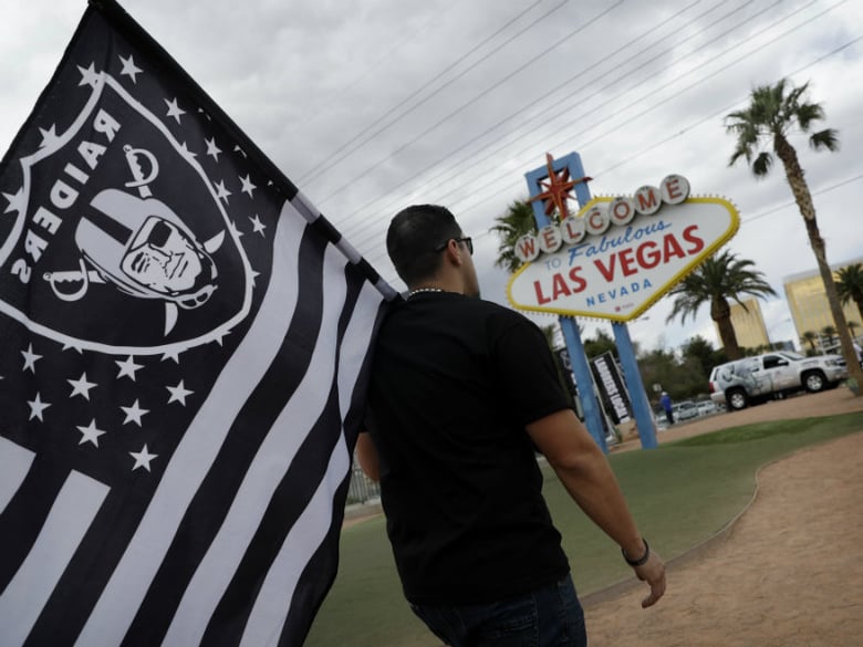 Matt Gutierrez carries a raiders flag by a sign welcoming visitors to Las Vegas, Monday, March 27, 2017, in Las Vegas. NFL team owners approved the move of the Raiders to Las Vegas in a vote at an NFL football annual meeting in Phoenix.  