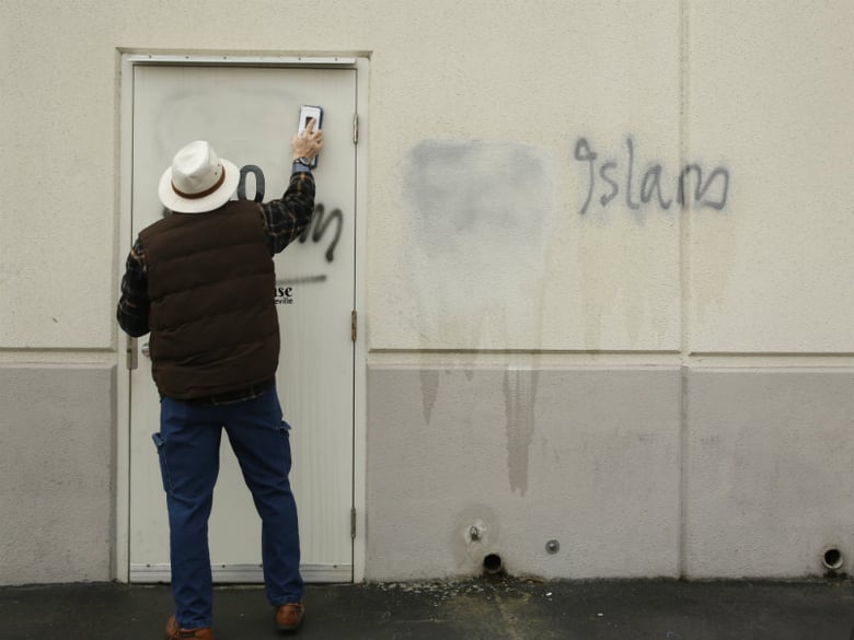 A volunteer cleans up racist graffiti painted on the side of a mosque in what officials are calling an apparent hate crime, Wednesday, Feb. 1, 2017, in Roseville, Calif. 