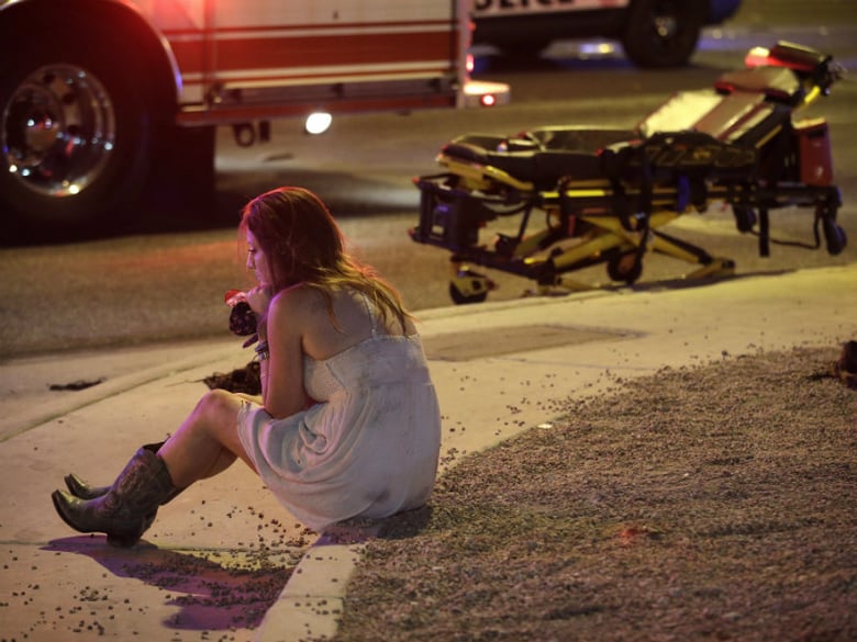 A woman sits on a curb at the scene of a shooting outside of a music festival along the Las Vegas Strip, Monday, Oct. 2, 2017, in Las Vegas. Multiple victims were being transported to hospitals after a shooting late Sunday on the Las Vegas Strip.