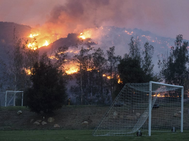 In this Sunday, Dec. 10, 2017, photo flames from a wildfire consume the mountainside near the Cate School campus in Carpinteria, Calif.