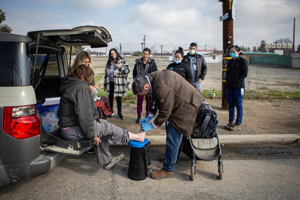 Dr. Mathew Beare treats a patient&rsquo;s foot along the side of the road outside Church Without Walls in Bakersfield on March 16, 2023. Photo by Larry Valenzuela, CalMatters/CatchLight Local